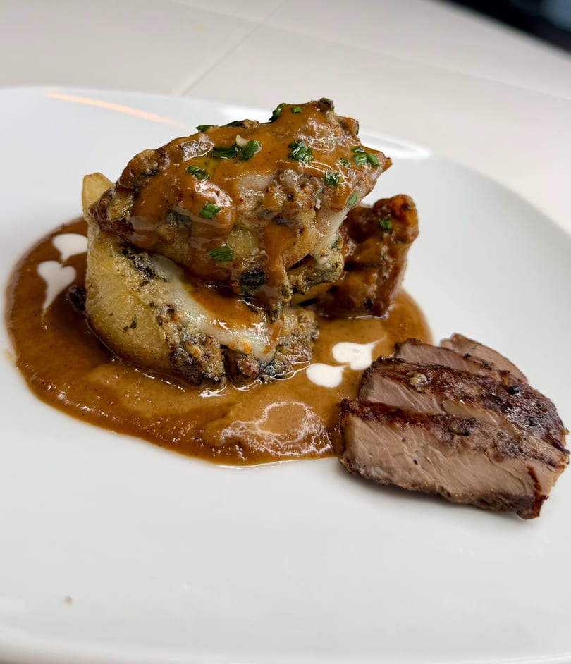 Stuffed chicken with sauce and sliced steak on a white plate with heart-shaped garnishes.